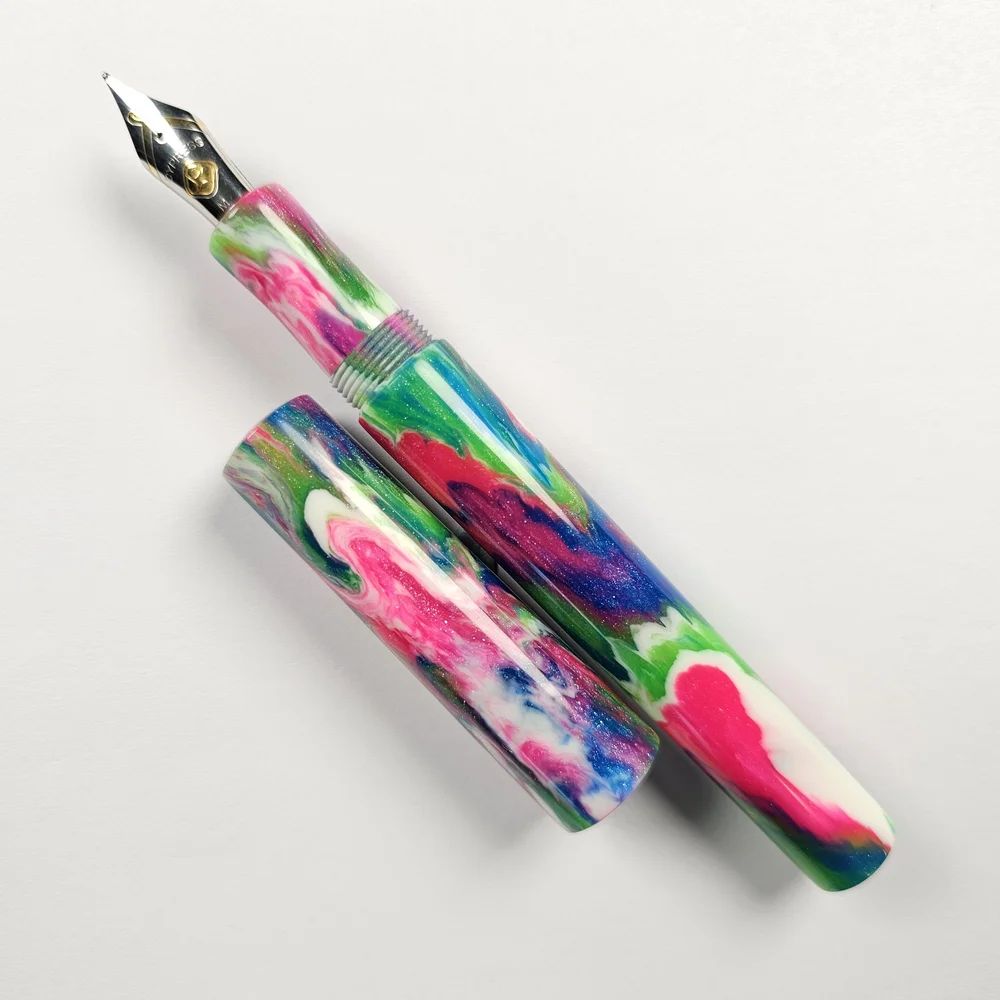 a hand-turned pen in glossy resin with an intricate pink, green, blue and white pattern