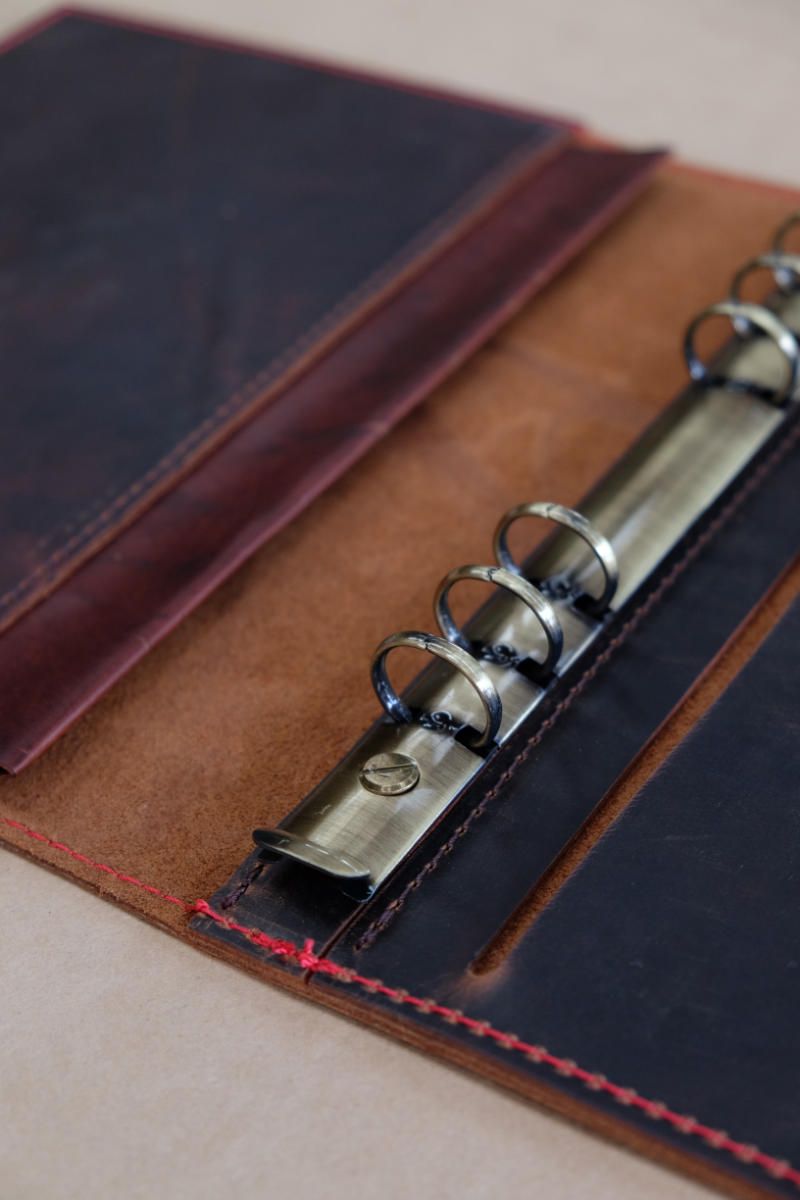 a leather notebook cover lying open, showing a ring binder on the spine