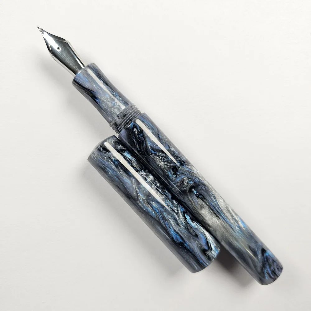 a hand-turned pen in glossy resin with an intricate blue, silver, and black pattern
