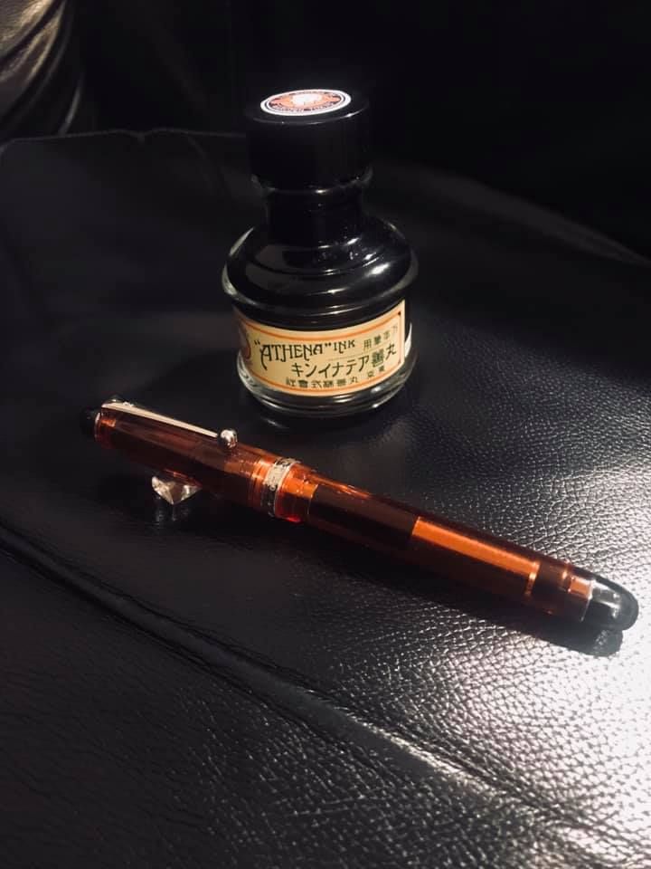 a translucent orange pen and a bottle of ink