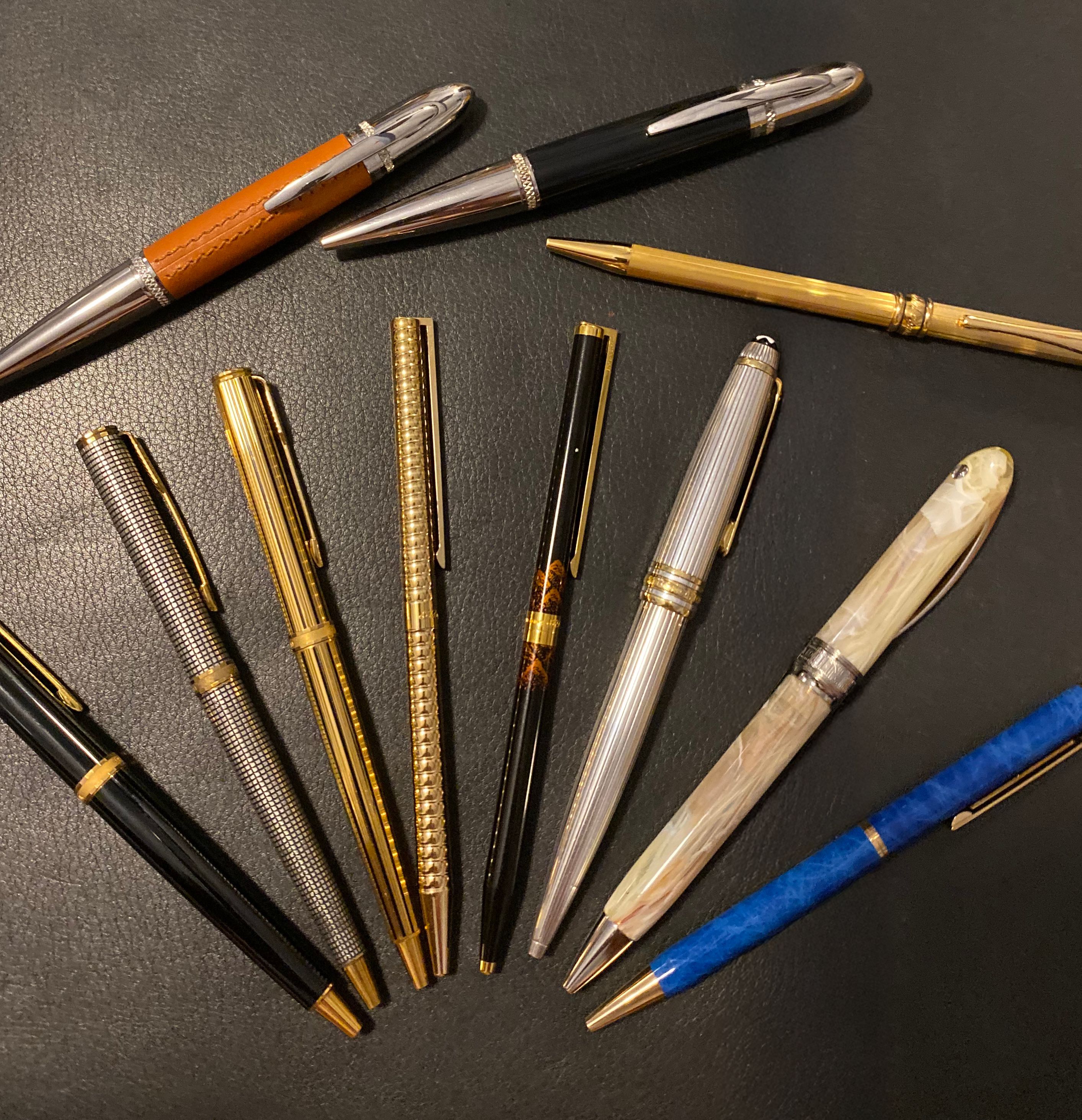 Eleven fountain pens spread in a fan shape on a black leather desk mat