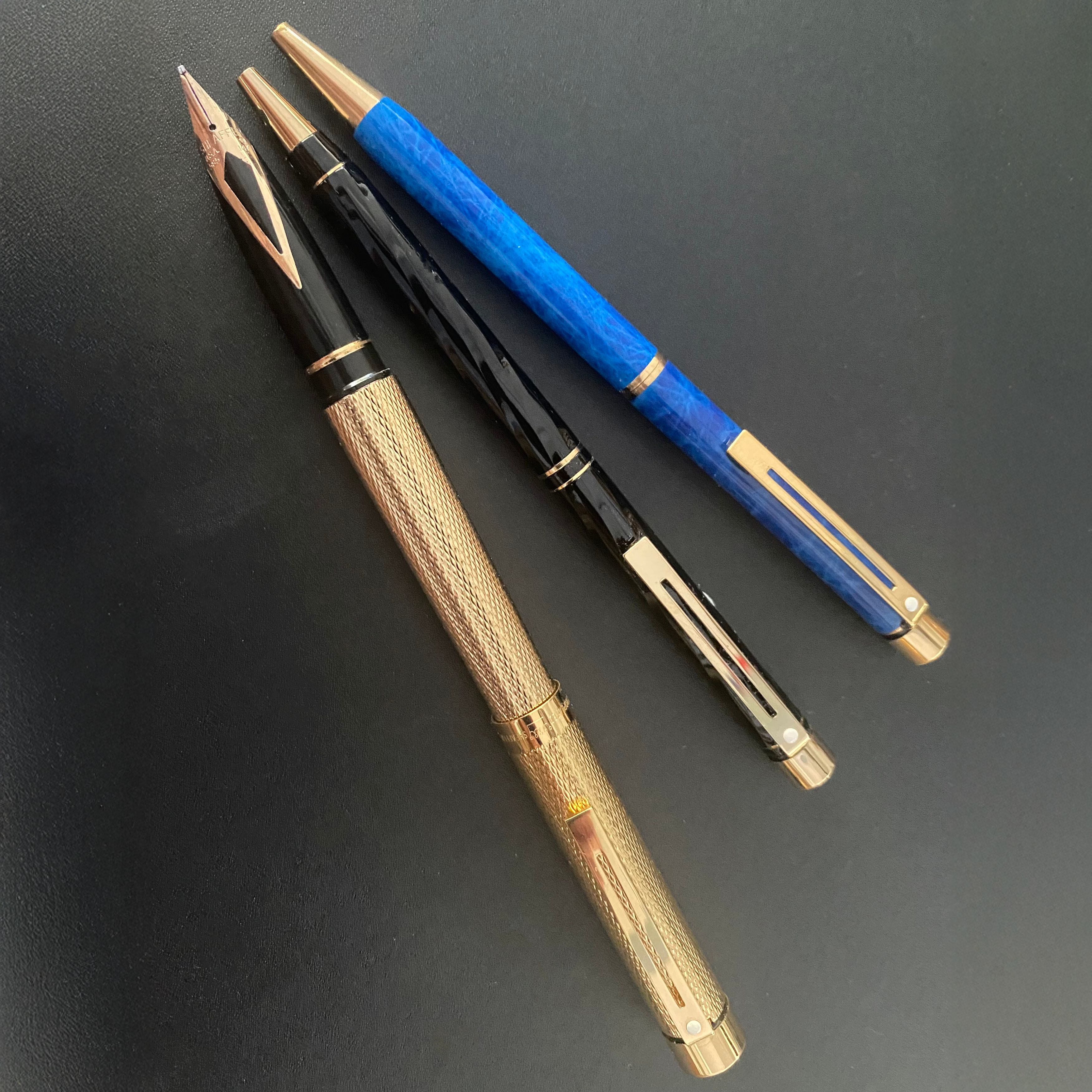 One fountain pen and two ball point pens on a black leather desk mat