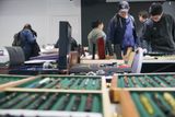 A collection of pens rest in green trays, out of focus in the foreground. In the background, visitors look down at items on the exhibitor's other tables.