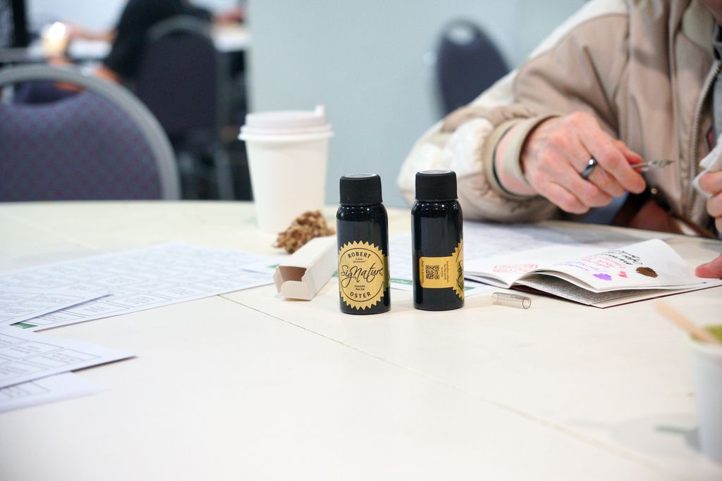 Two bottles of Robert Oster ink sit on a table next to a visitor's open notebook, with ink swatches on the page.