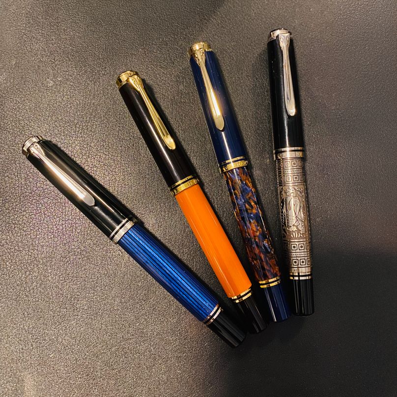 Four Pelikan fountain pens spread in a fan on a black leather desk mat