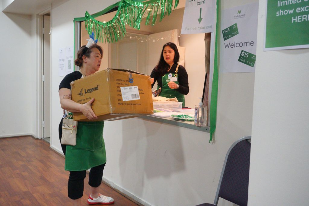 A volunteer in a green apron delivers a large cardboard box to the reception desk