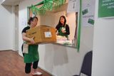 A volunteer in a green apron delivers a large cardboard box to the reception desk