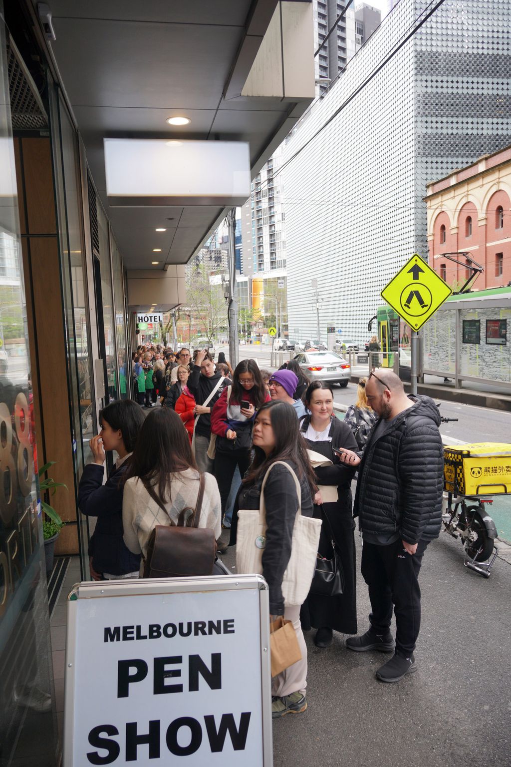 A long queue of people down the sidewalk, ending at a door with a