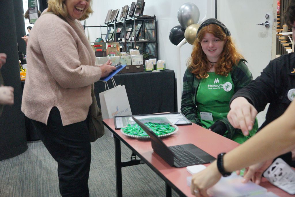A happy guest and a volunteer in a green apron at the Info desk