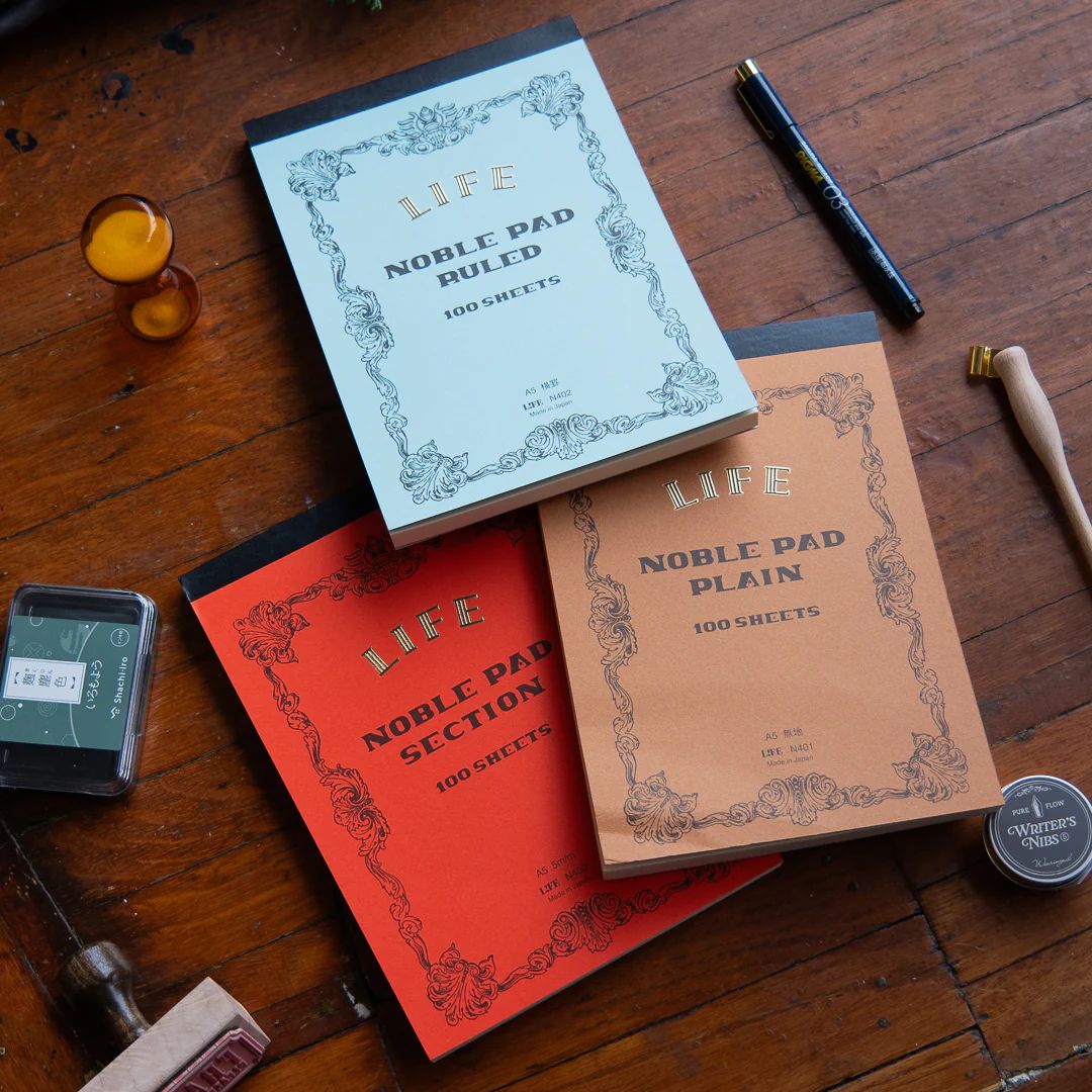 Life brand notebooks surrounded by pens, stamps, and other desk accoutrement
