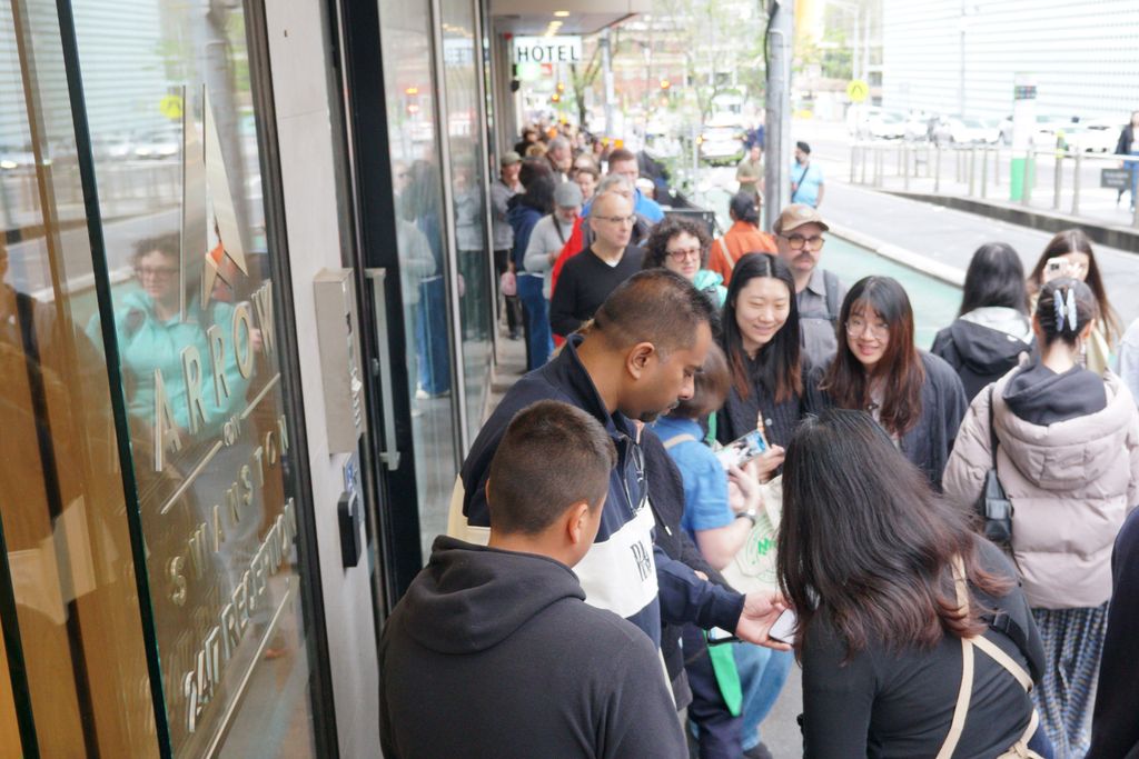 In the queue on the sidewalk, a group of visitors look at one of their phones