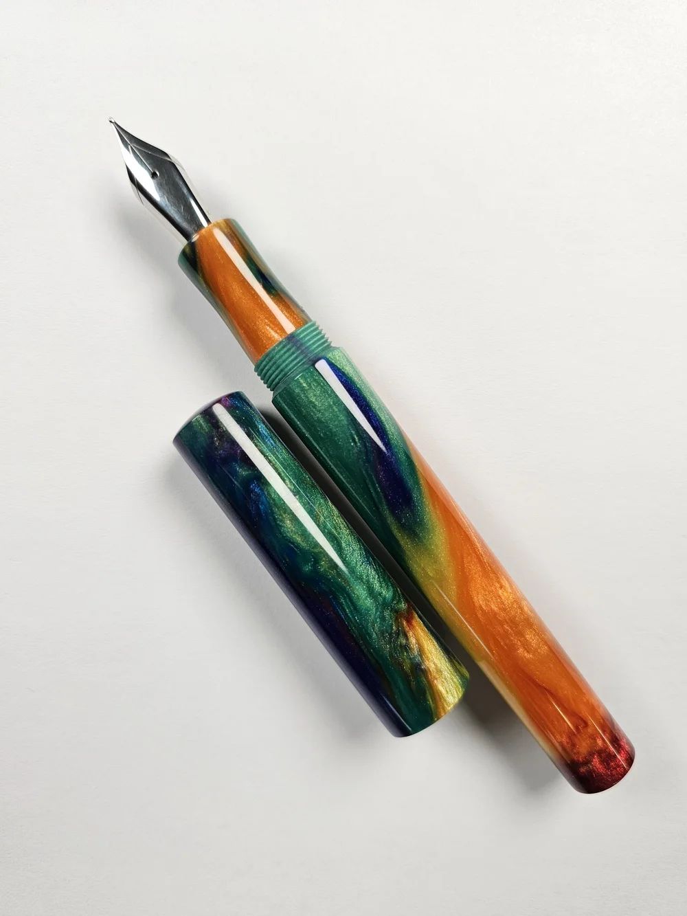 a hand-turned pen in glossy resin with an intricate green, yellow, and orange pattern