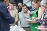 A group of guests at an exhibitor's table, including one volunteer in a green apron who photographs a page with her phone