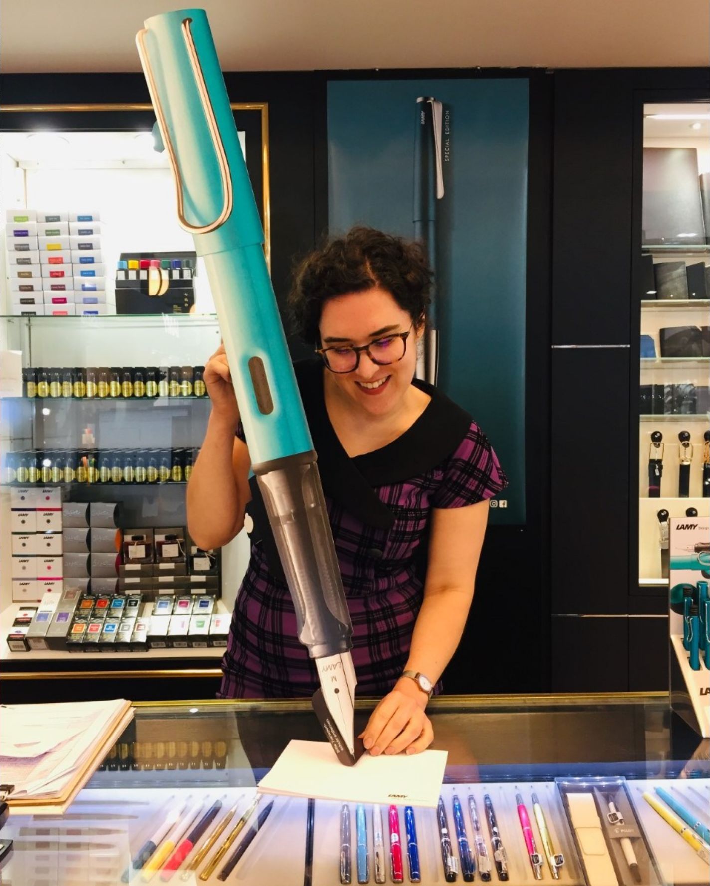 PtB staff holding a giant novelty size Lamy fountain pen, pretending to write with it. Wimsy!