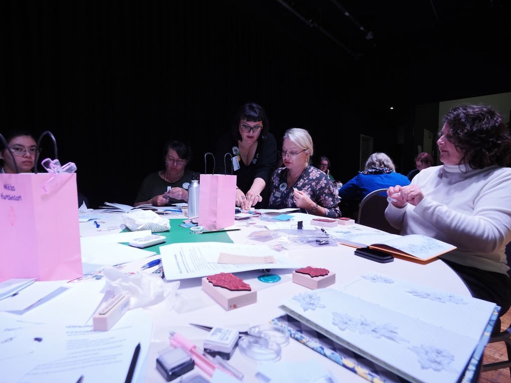 With a table full of journals-in-progress in the foreground, Dina helps a workshop participant at one of the tables