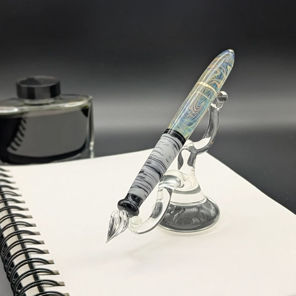 Borosilicate glass dip pen, with half-half colour, bottom half solid black glass with concentric white streaks, top half clear glass with crazy chaotic blue and yellow pattern