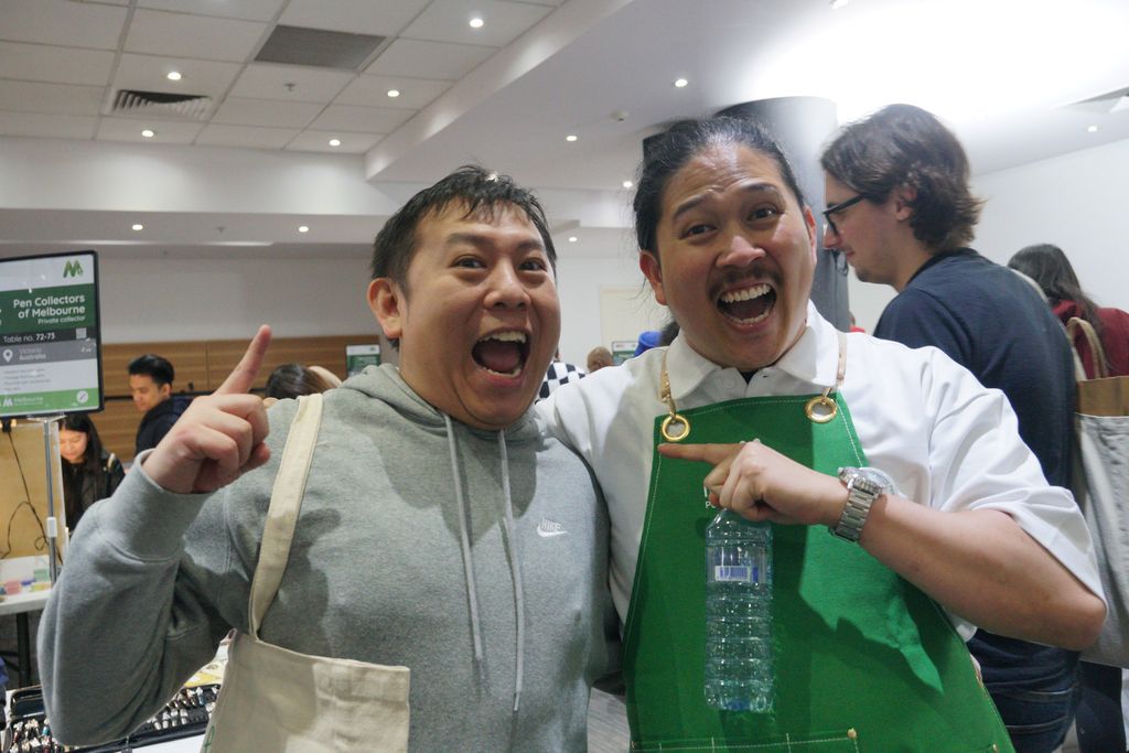 A volunteer and a visitor with excited expressions. The volunteer, wearing a green apron points at the visitor. The visitor points at the ceiling.