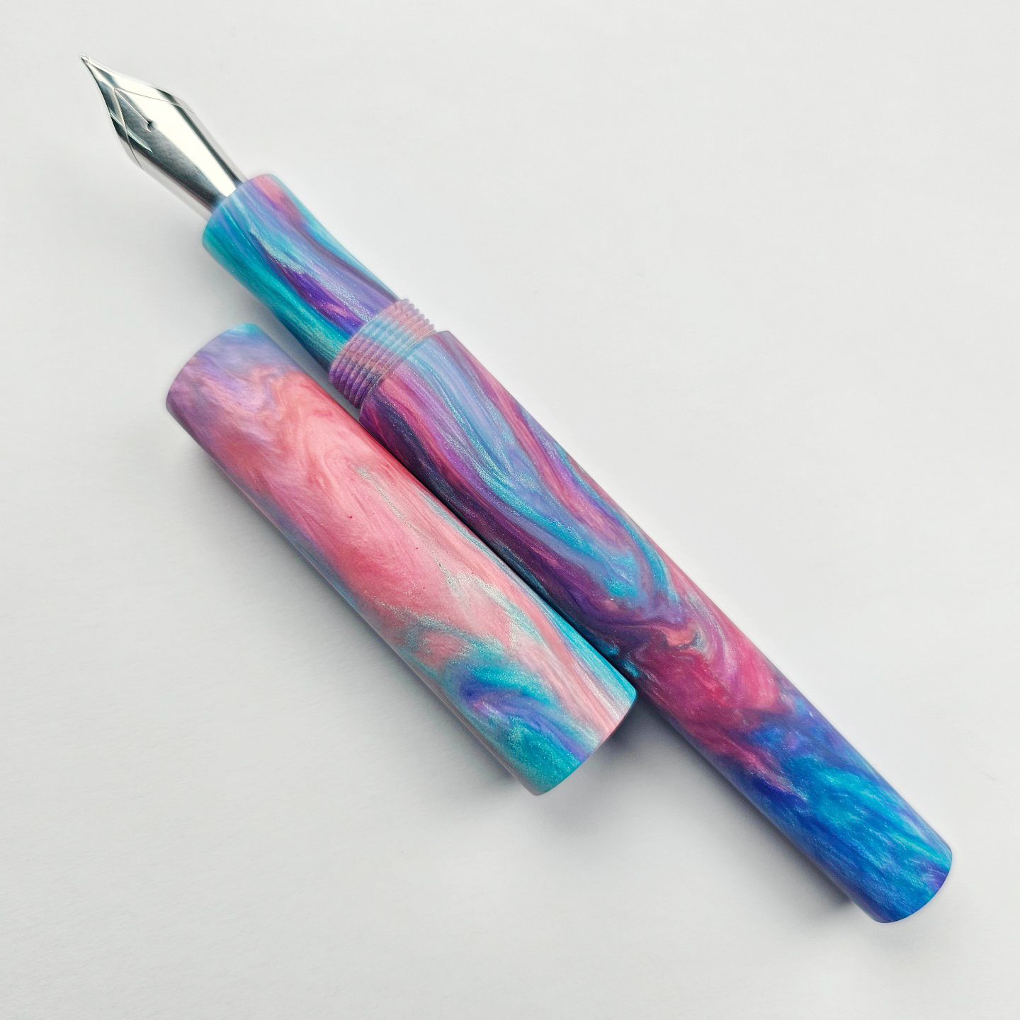 a hand-turned pen in glossy resin with an intricate pink, blue, and purple pattern