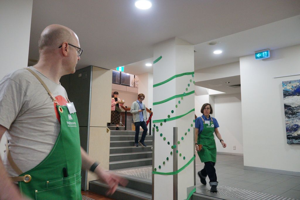 Two people in green aprons cross paths at the bottom of a stairwell