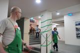Two people in green aprons cross paths at the bottom of a stairwell