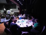Workshop participants work around large, round tables up on the stage