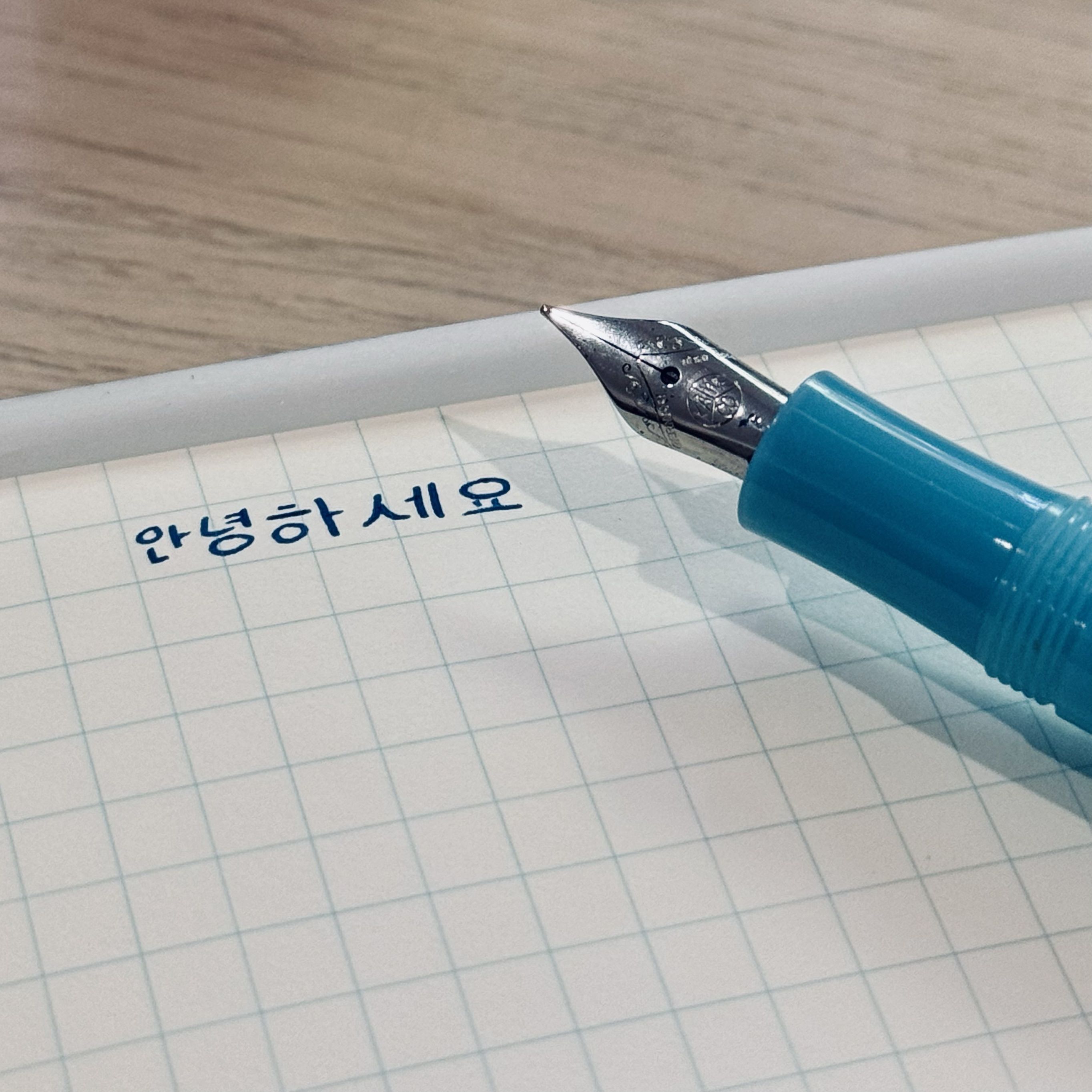 Turquoise Kaweco fountain pen, on a grid notebook, with Korean Hangul handwriting