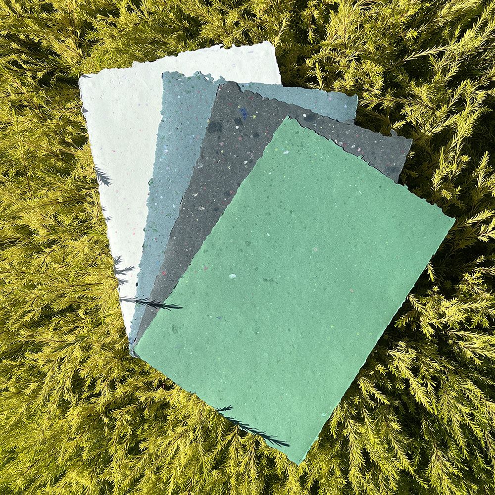 Four sheets of textured, colourful recycled paper in white, blue, grey, and green