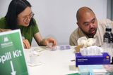 Two visitors look with excitement at their purchases on a white table. A sign saying